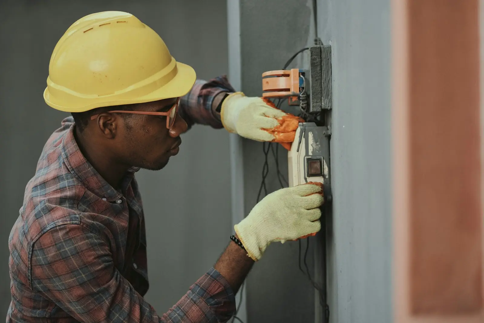 Electrician in a safety helmet repairing wall wiring during maintenance